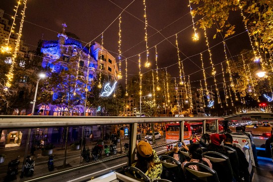 Gente che ammira le luminarie e la facciata di Casa Batllò da una prospettiva molto ravvicinata, comodamente seduta sul piano superiore del Barcellona Christmas Tour Bus