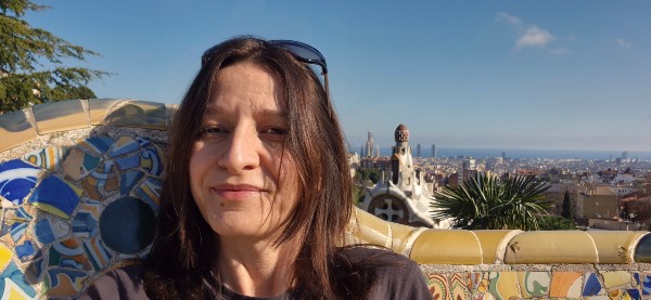 Primo piano di Lory seduta sulla panca colorata di Parc Guell con vista panoramica su Barcellona alle spalle