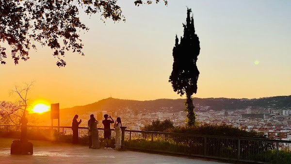 un piccolo gruppetto di persone in controluce che ammira il tramonto su Barcellona dal Mirador de Miramar sul Montjuic